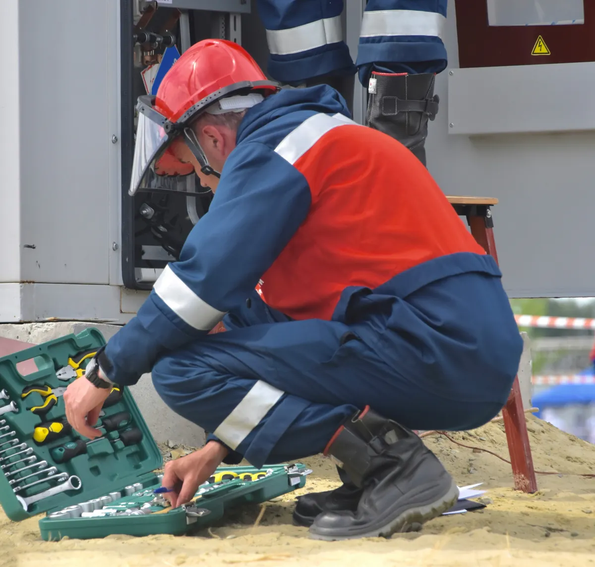 Technician in safety gear opening his toolkit at an electrical panel